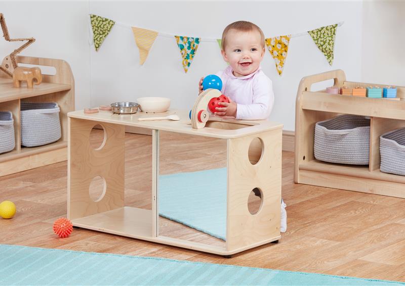 An toddler standing against the Under 2’s Activity Kitchen and smiling
